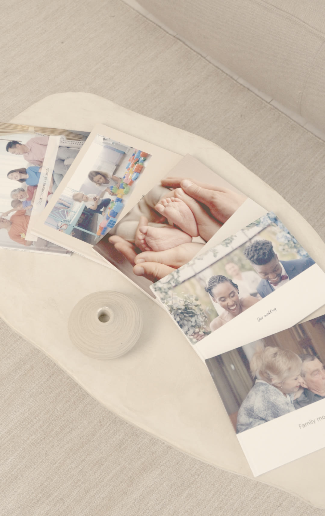 Nokoru photobooks fanned out on a pale stone table beside a small ceramic vase, with a family, a baby's feet, a wedding and an older couple on their covers