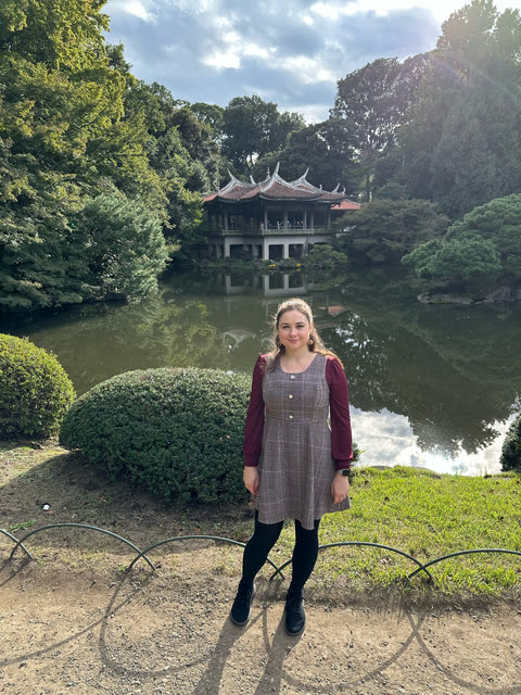Me standing by a pond in a garden, with a pavilion among the trees behind me